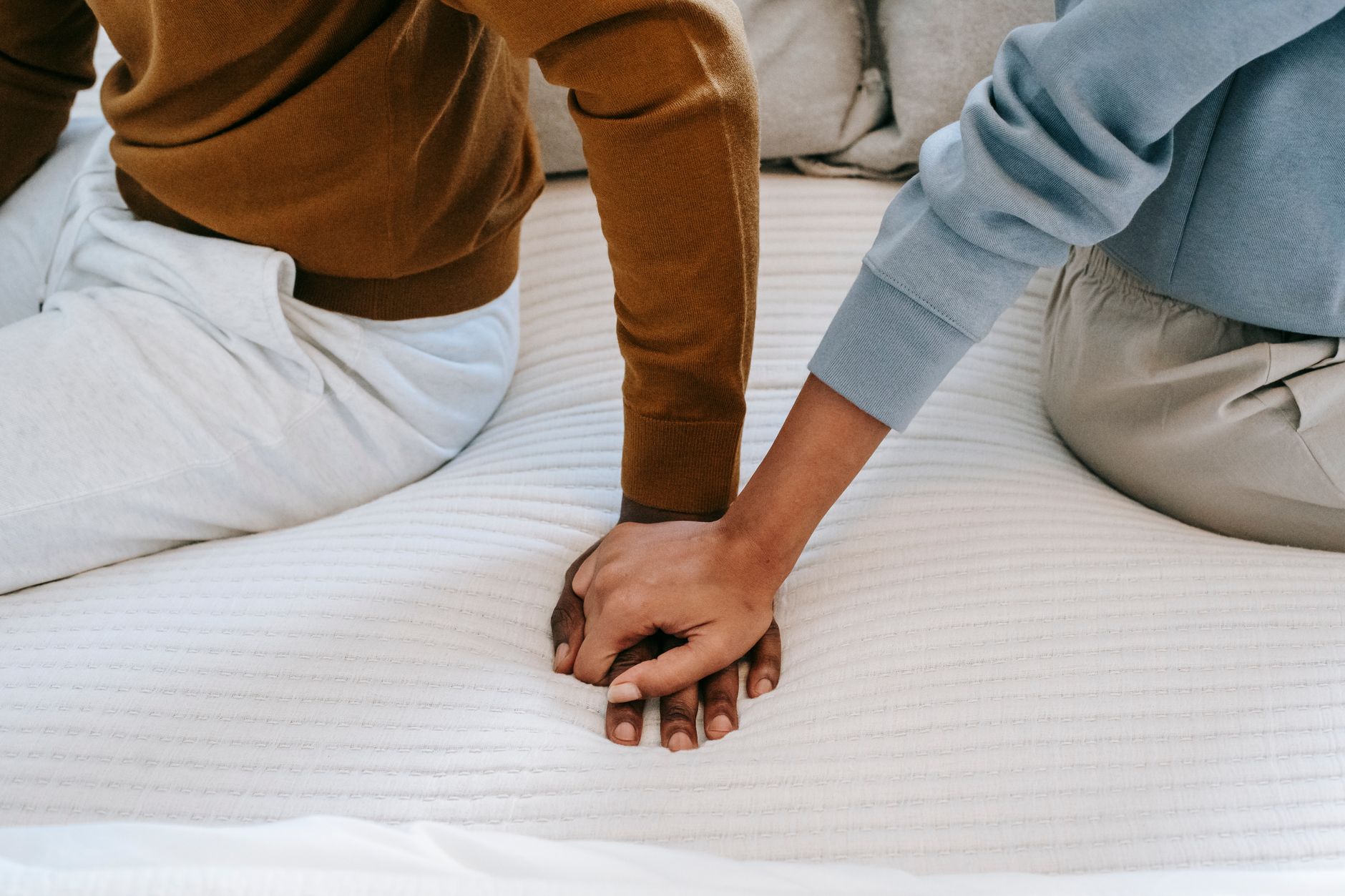 Twee partners zitten op bed en houden elkaars hand vast